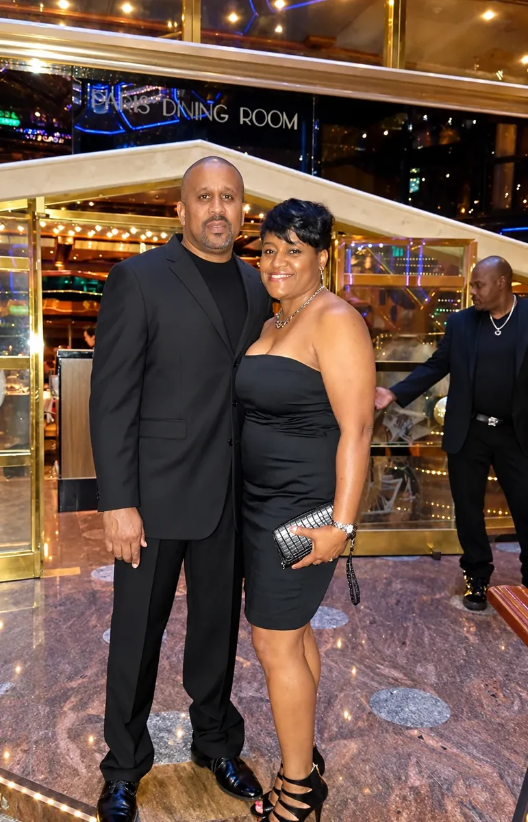 Couple in black formal attire posing beside the dining room in a cruise ship atrium