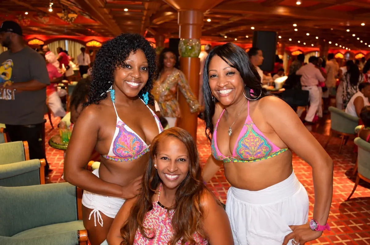 Three friends in coordinated pink patterned outfits smiling in a cruise ship lounge